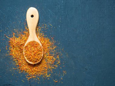Siyah arka planda, tahta kaşıkta kurumuş safran baharatları.