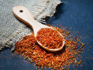 Siyah arka planda, tahta kaşıkta kurumuş safran baharatları.