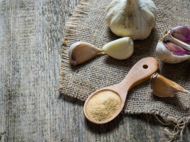 Lezzetli sarımsak soğanları ve karanfiller bir kaşık dolusu sarımsak tozu ile ahşap bir masada