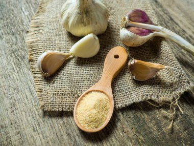 Lezzetli sarımsak soğanları ve karanfiller bir kaşık dolusu sarımsak tozu ile ahşap bir masada