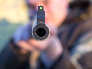 Bir adam objektife nişan alıyor, havalı tüfeğin namlusuna yakın plan.