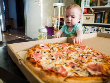 Küçük bir çocuk bir dilim pizzaya uzanır.