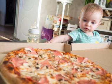 Küçük bir çocuk bir dilim pizzaya uzanır.