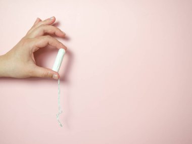 Bir kadının eli, pembe arka planda temiz bir pamuk çubuğu tutar. Tıbbi hijyen kavramı