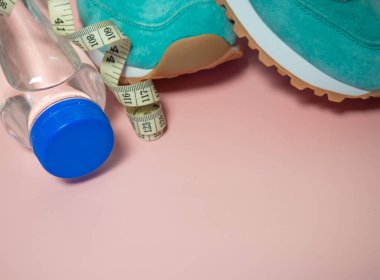 Turkuaz spor ayakkabılar ve pembe arka planda bir şişe su. Sağlıklı yaşam tarzı, günlük eğitim ve figürleri takip etme kavramı. 