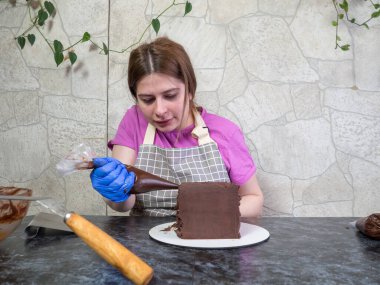 Pasta şefi kız ganache sürülmüş çikolatalı kek yapıyor.