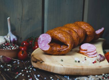 Yüzük, ahşap kesme tahtasındaki füme domuz sosisi sarmalı, baharatlar, domatesler, geleneksel sosis, eski tarifler.