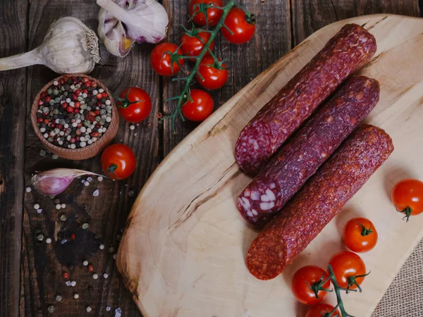 different types of salami on a wooden board with spices and cherry tomatoes