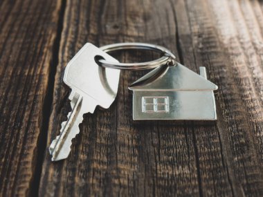 Ev anahtarı ve anahtarlık bir ev şeklinde, tahta bir arka planda, mesaj için bir yer. Gayrimenkul, eve taşınma ya da emlak kiralama kavramları