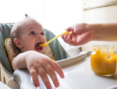 Baba bebeğe bir kaşık sebze püresi verir. Çocuk yer.