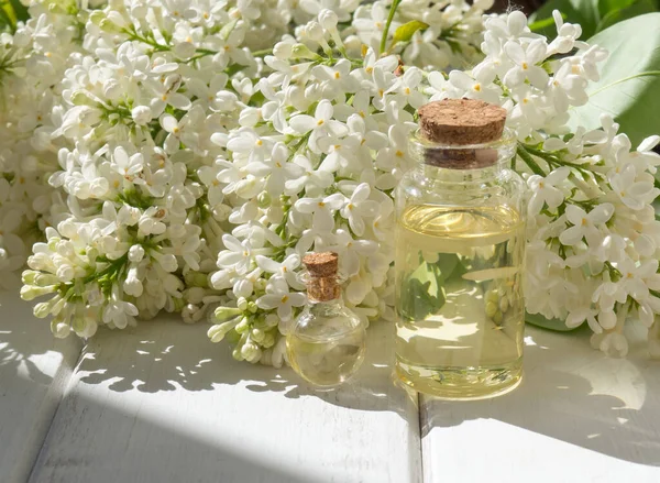 Spa oil with lilac flowers. A bottle of aromatic oil and white lilac flowers on a wooden background