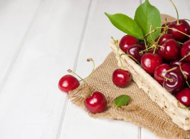 fresh cherries in a wicker basket on a white wooden table