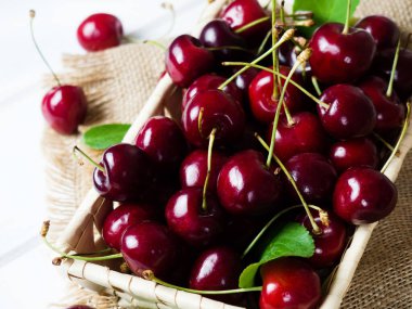 fresh cherries in a wicker basket on a white wooden table