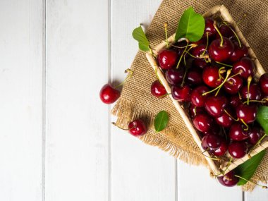 fresh cherries in a wicker basket on a white wooden table