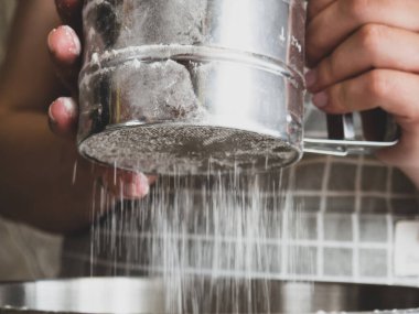 The girl's hand holds a metal sifter of flour, flour is sprinkled through a sieve. Sifting flour. Preparation for baking.
