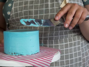 Pasta şefi kız, yeni pişmiş doğum günü pastasına spatula sürerek krema sürüyor.