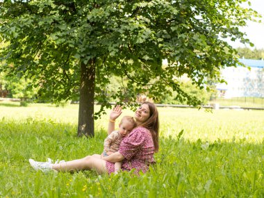 beautiful young mother with a baby in her arms sits in the park on the grass on a sunny day