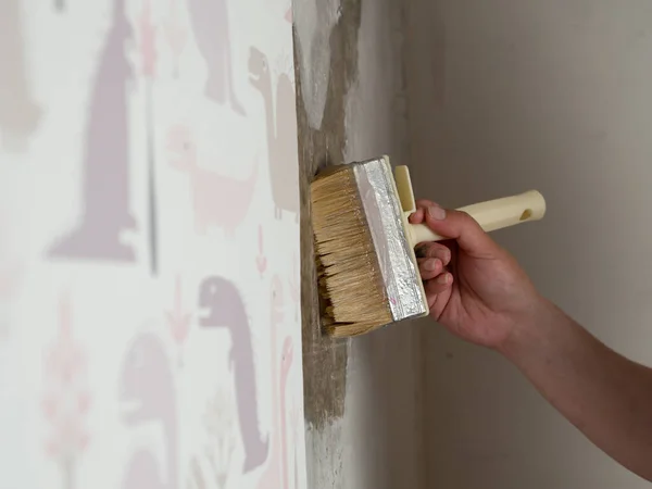 girl glues children's wallpaper on the wall, smears the wall with glue with a brush