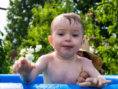 Güzel bir kız çocuğu sıcak bir günde annesiyle şişme bir havuzda banyo yapar ve oynar.