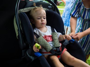Anne çocuğu çocuk oto koltuğuna oturtuyor.