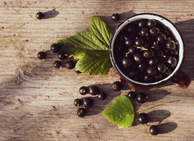 Kupada siyah frenk üzümü ve ahşap bir masaya serpiştirilmiş.