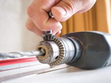 Tahta bir masada matkabın matkabını değiştiren bir adamın eli. Onarım konsepti. Kopyalama alanı olan resim.