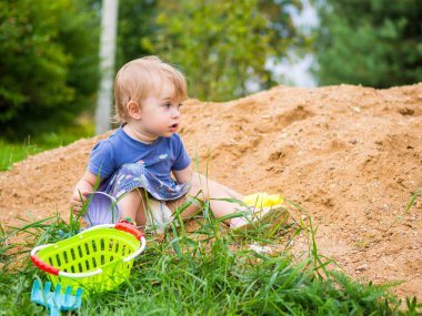 Güzel bir kız çocuğu kum havuzunda oynuyor.