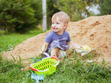 Güzel bir kız çocuğu kum havuzunda oynuyor.