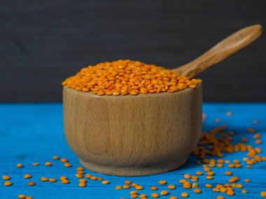 Tahta bir tabakta kırmızı mercimek ve eski bir kırsal masada kaşık. Vejetaryen yemeği..