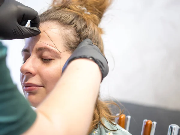 Make-up artist plucking eyebrows with a thread Professional face care.