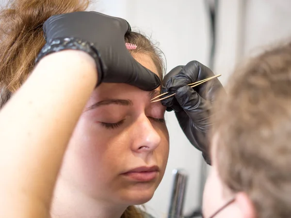 Permanent makeup. Beautiful young woman receiving eyebrow correction procedure. Tweezing a girl's eyebrows with tweezers