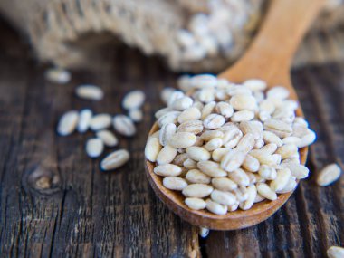 Tahta bir kaşıkta çiğ inci arpası Eski bir ahşap masaya dökülüyor