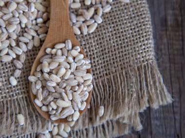 Tahta bir kaşıkta çiğ inci arpası Eski bir ahşap masaya dökülüyor