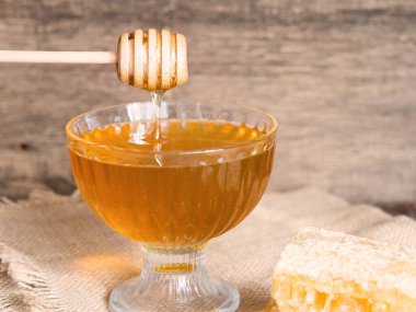 Bal damlaları bal kabından güzel bir cam kaseye damlıyor. Yakın plan. Sağlıklı organik, kalın bal ve tarak.