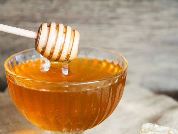 Honey drips from a honey dipper into a beautiful glass bowl. Close-up. Healthy organic thick honey and combs.