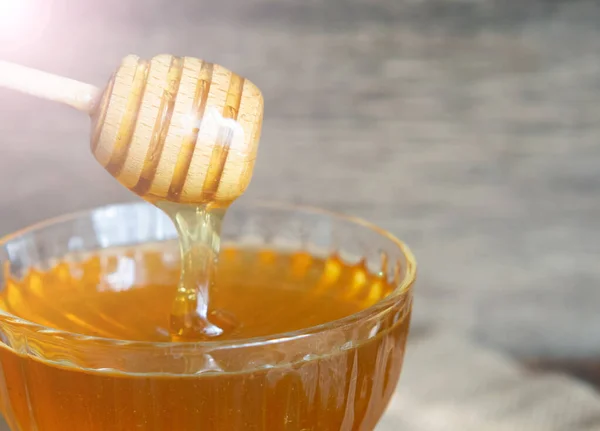 Honey drips from a honey dipper into a beautiful glass bowl. Close-up. Healthy organic thick honey and combs.