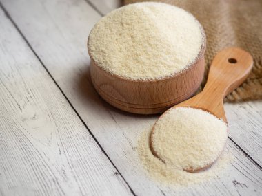 Semolina ahşap bir kasede ve kaşıkla beyaz tahta bir masada, yakın plan. Sağlıklı beslenme mısır gevreği arka planı.