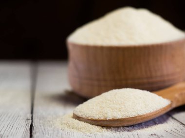 Semolina ahşap bir kasede ve kaşıkla beyaz tahta bir masada, yakın plan. Sağlıklı beslenme mısır gevreği arka planı.