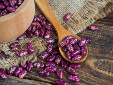 Şablonlu kırmızı fasulyeler. (Lezzetli çeşitlilikte, çiğ fasulye) eski ahşap bir masanın üzerinde yakın plan bir tahta kaşık, baklagiller. Boşluğu kopyala