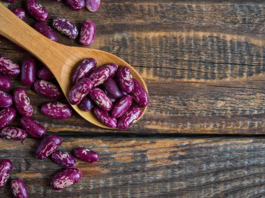 Şablonlu kırmızı fasulyeler. (Lezzetli çeşitlilikte, çiğ fasulye) eski ahşap bir masanın üzerinde yakın plan bir tahta kaşık, baklagiller. Boşluğu kopyala