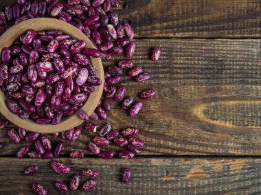Şablonlu kırmızı fasulyeler. (Lezzetli çeşitlilik, çiğ fasulye) eski ahşap bir masa üzerinde ahşap bir kase, baklagiller. Boşluğu kopyala