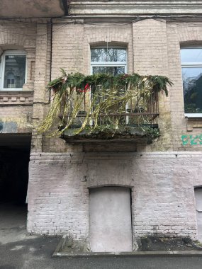 Yeşil dalları ve altın süslemeleri olan küçük bir balkonu olan eski tuğladan bir bina.