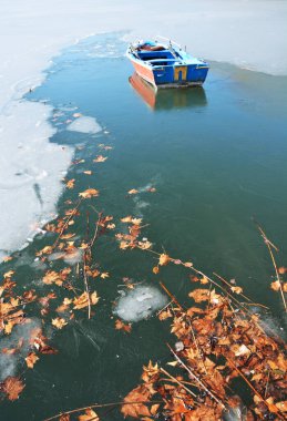 Yunanistan 'ın Kastoria kentindeki Orestiada Gölü' nün buzlu sularında sıkışmış uçak ağacı yaprakları ve balıkçı teknesi