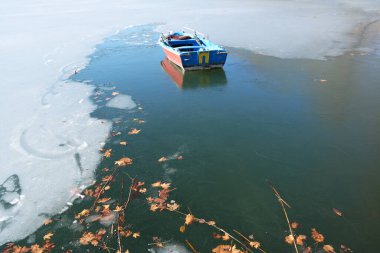 Yunanistan 'ın Kastoria kentindeki Orestiada Gölü' nün buzlu sularında sıkışmış uçak ağacı yaprakları ve balıkçı teknesi