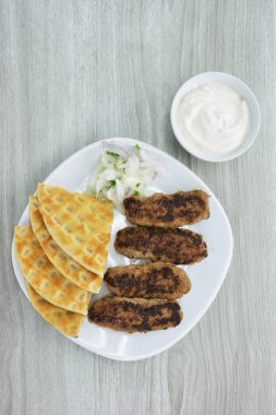 Pide ekmekli ızgara kebap, doğranmış soğan ve yoğurt sosu ahşap masada.