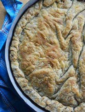 Geleneksel Yunan ıspanaklı peynirli turta fırın tepsisi ve mutfak havlusunun yanında ahşap hamurlu rulo tahtada