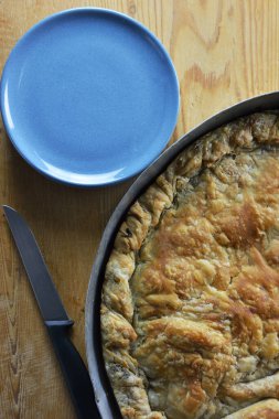Geleneksel Yunan ıspanak peynirli turta fırın tavasında, tabaklar ve bıçak ahşap hamurun üzerinde yuvarlanıyor.
