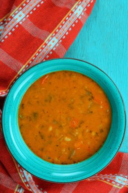 Kırmızı mutfak havlusu ve turkuaz masa üzerinde beyaz fasulye çorbası.