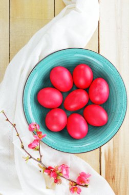 Turquoise bowl with red eggs and branch of flowering quince on wooden table