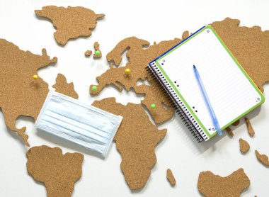 Bir salgın sırasında seyahat kavramı, bir dünya haritası ve kişisel koruma aracı olarak maske, tarafsız arka planda düz yatıyordu